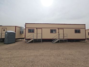 Two beige portable trailers in a gravel lot under a cloudy sky.
