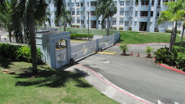 Gated entrance to a residential complex with palm trees and white buildings.
