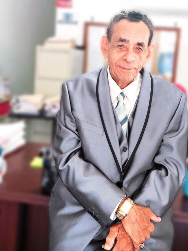 Elderly man in a gray suit smiling warmly indoors.
