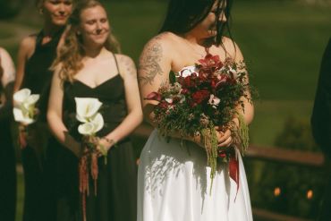 Bride in white dress holding a bouquet, with bridesmaids in black dresses behind her.