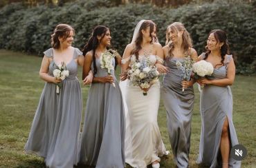 Bride and bridesmaids in elegant dresses walking outdoors, holding bouquets.