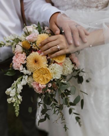 Newlyweds' hands with wedding ring and bouquet of flowers.