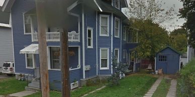 Blue two-story house with a small shed and green lawn.