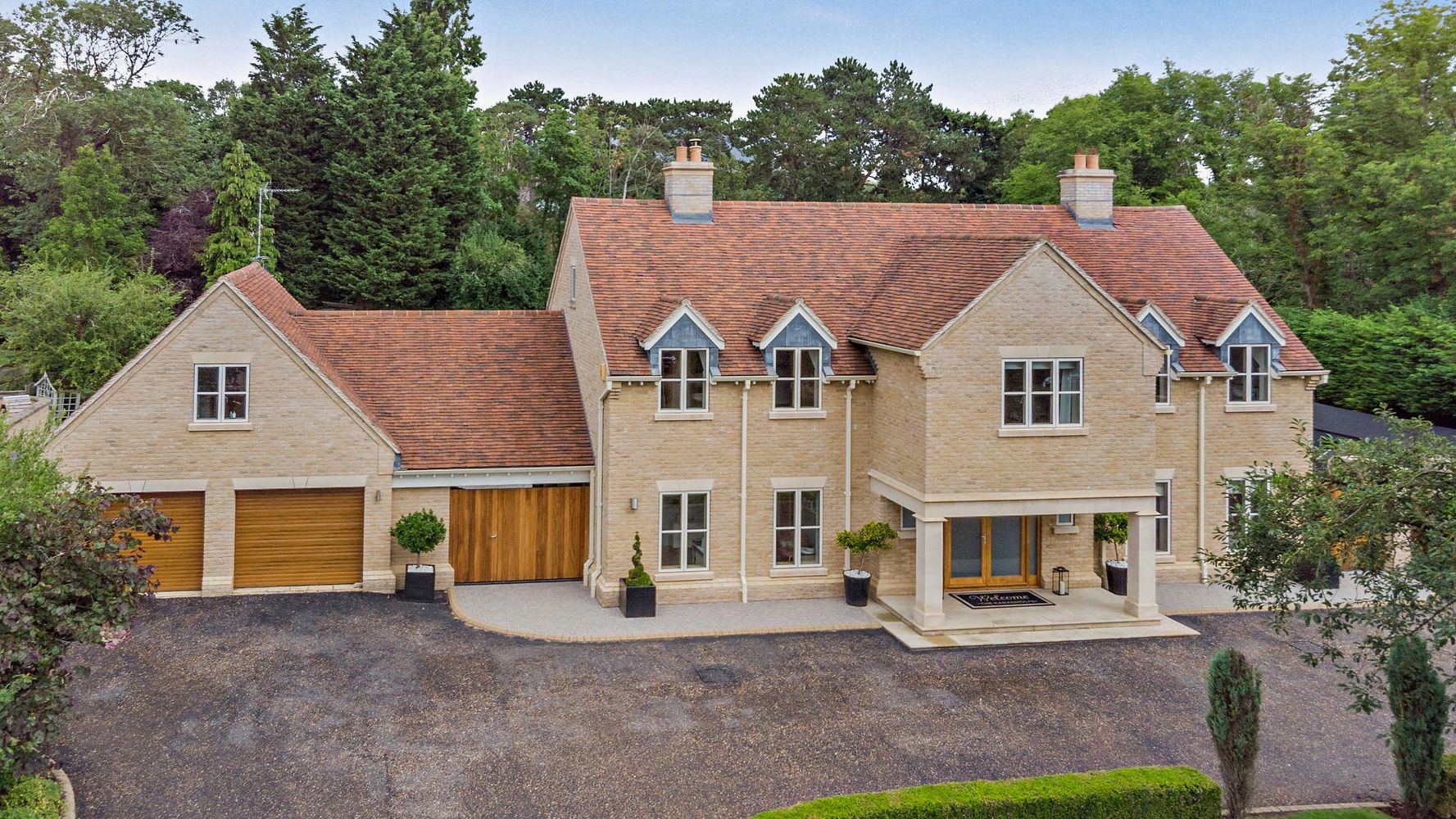 Large modern house with red tile roof and multiple garages surrounded by greenery.