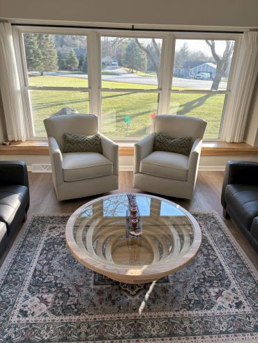 Two beige armchairs and a reflective round glass table in a cozy living room.