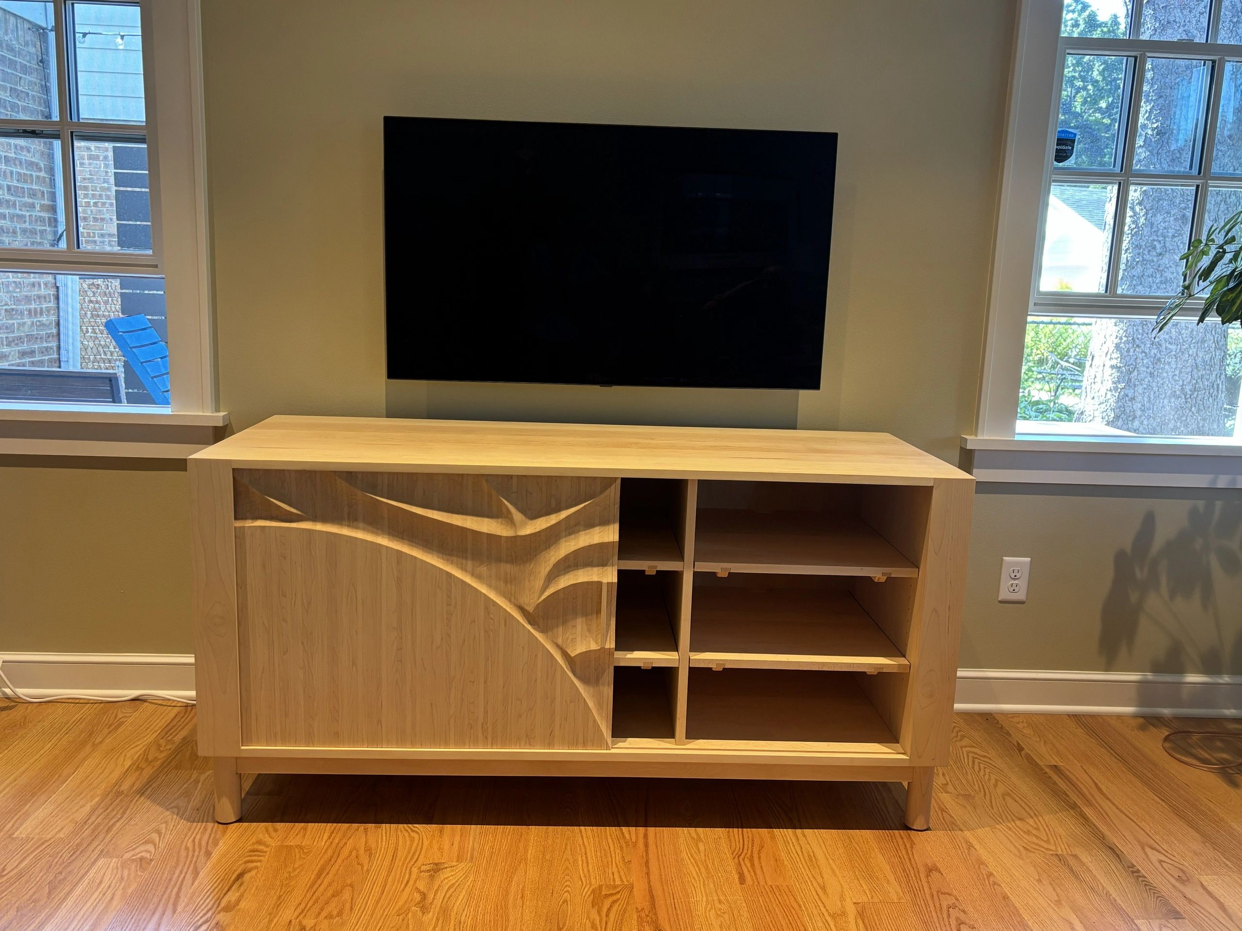 Modern TV setup with wooden cabinet and large windows.