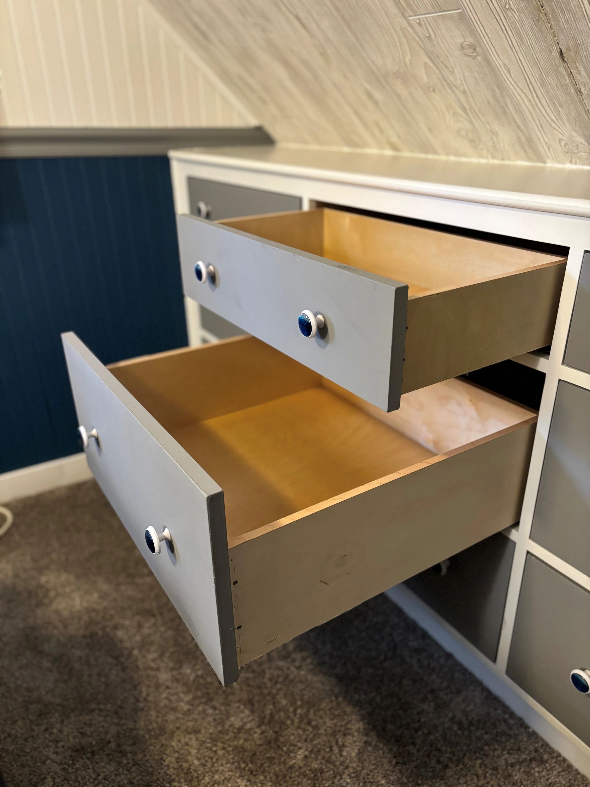 Open drawers of a gray dresser with blue knobs.