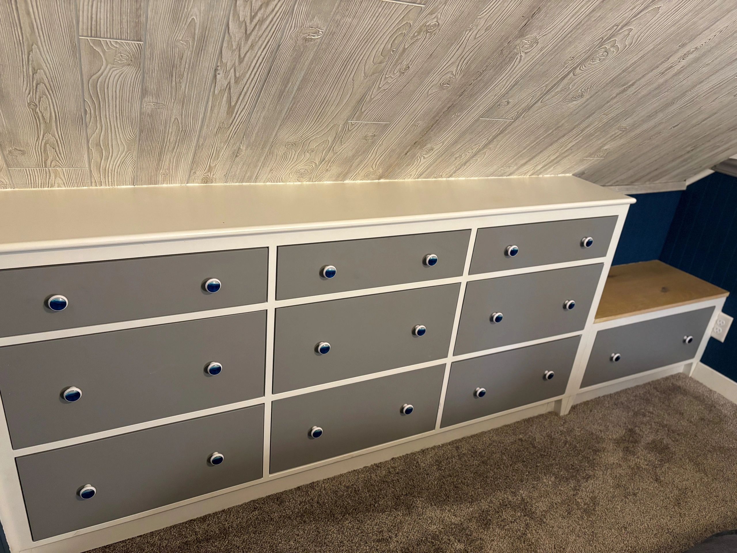 Gray and white drawers with blue knobs under a wood-paneled ceiling.