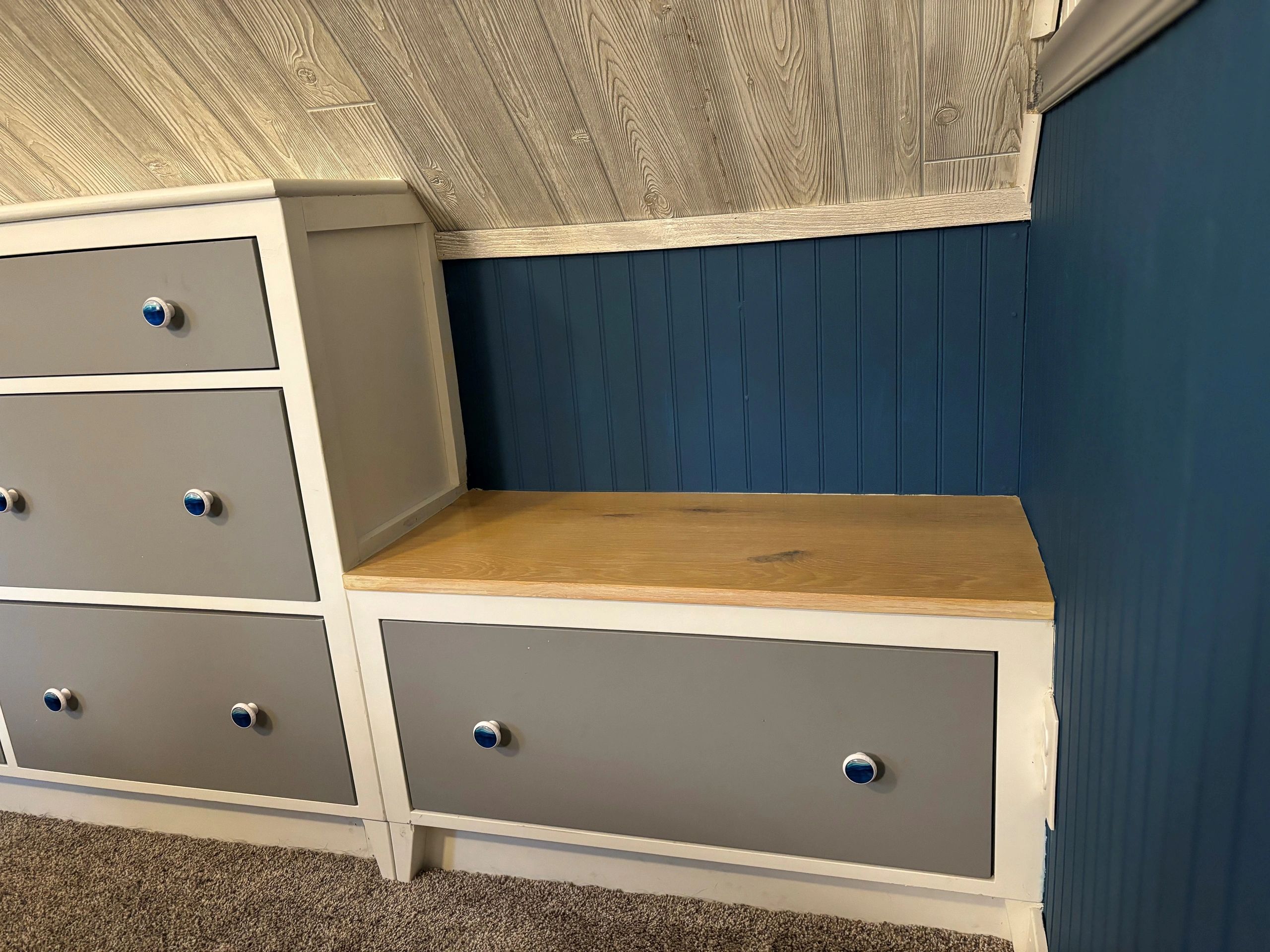 Gray drawer dresser with blue knobs against a blue wall.