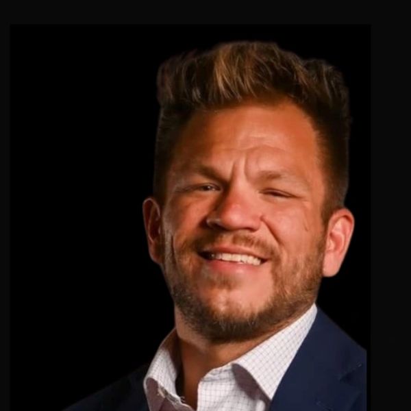 Smiling man in a blue suit and white shirt against a black background.