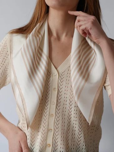 Woman wearing a cream knitted cardigan and a striped silk scarf.