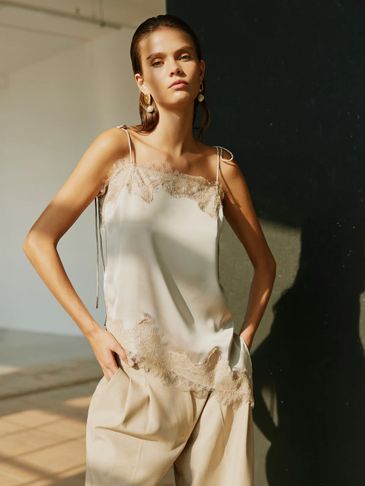 Woman in elegant beige lace-trimmed top and loose pants posing indoors.