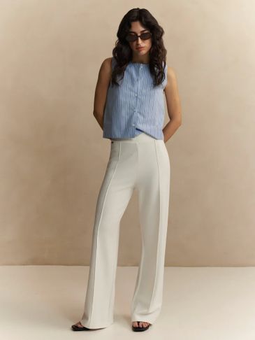 Woman wearing a sleeveless blue striped top and white high-waisted pants.