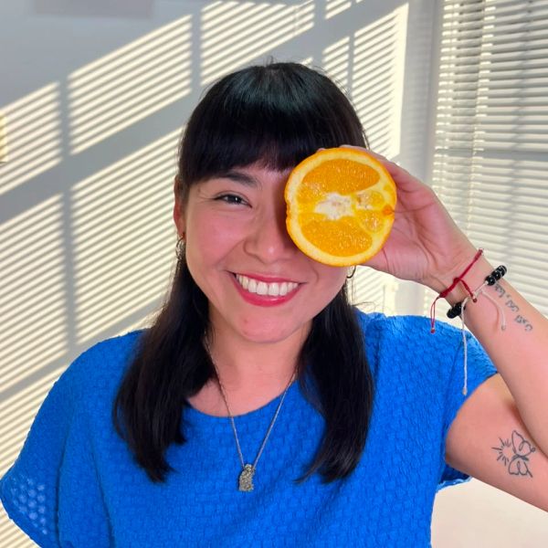 Mujer sonriente con una naranja cubriendo un ojo.