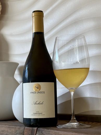 Bottle of Chardonnay wine with a filled wine glass on a wooden surface.