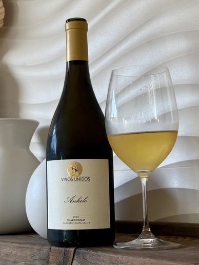 Bottle of Chardonnay wine with a filled wine glass on a wooden surface.