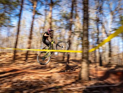 Cyclist performing a jump on a mountain bike in a forest trail.