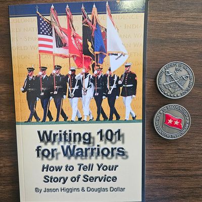 A book titled 'Writing 101 for Warriors' and two military challenge coins on a wooden surface.