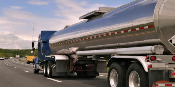 A blue semi-truck hauling a shiny tanker on a highway.