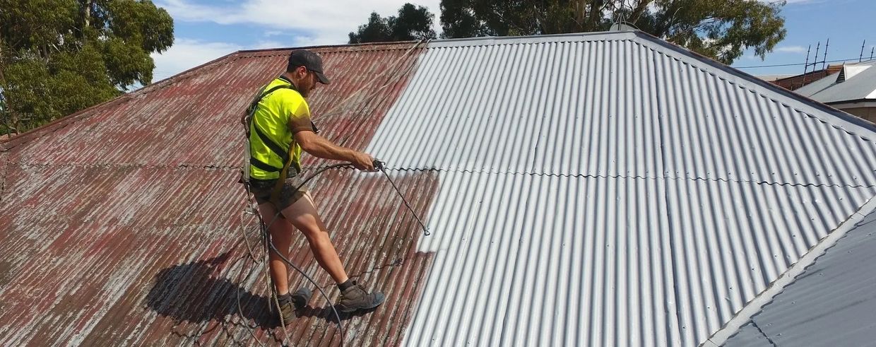 Roofing contractor pressure washing on a tin roof a residential home
