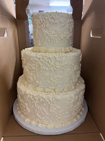 Three-tier white cake with intricate floral icing designs.