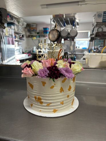 Elegant birthday cake with flowers and gold accents on a kitchen counter.