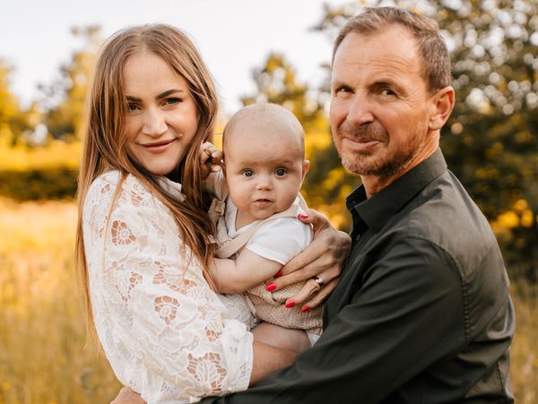 A happy family of three posing outdoors with warm sunlight.