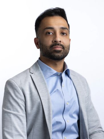 Professional man in light grey blazer and blue shirt against white background.