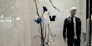 Store window display with a mannequin and artistic blue flowers on branches.