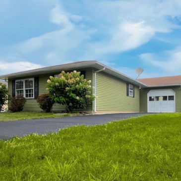 Single-story green house with attached garage on grassy lawn.