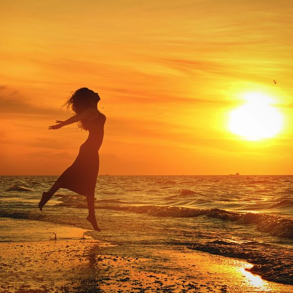 A woman joyfully jumps on the beach during a golden sunset.