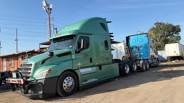 Two large semi trucks parked on a dirt lot under a clear sky.