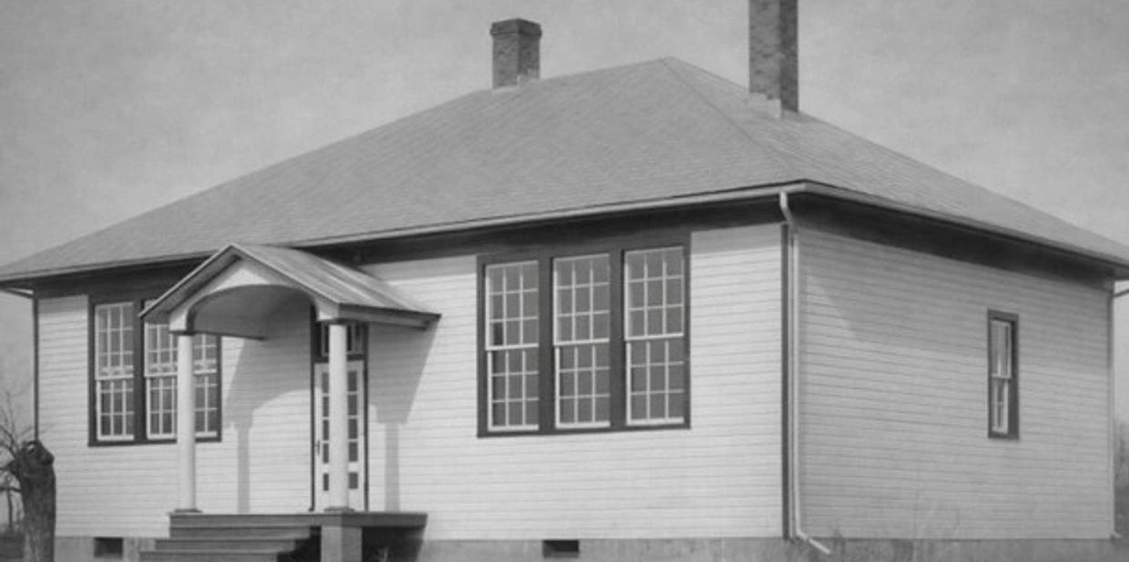 Black and white photo of a simple, early 20th-century wooden house with a small porch.