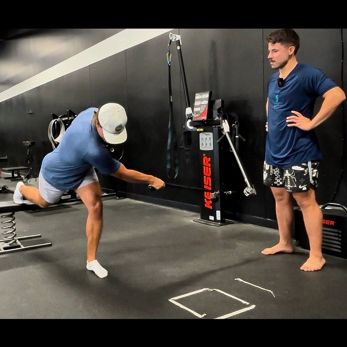 Man performing a balance exercise with resistance band under coach supervision.