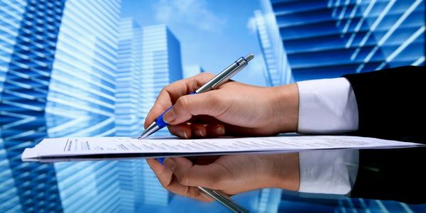 A businessperson signing a document with city skyscrapers reflected on a glossy surface.