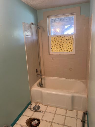 Small bathroom with a bathtub, window, and tiled walls.