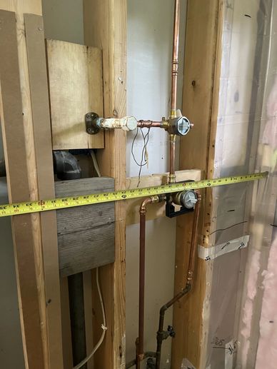 Measuring copper plumbing pipes inside a wooden wall frame during installation.