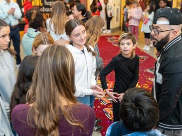 A group of kids talking to a man in a crowded room.