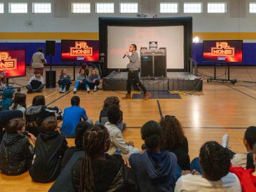 Speaker presenting to an attentive group of students in a gym.
