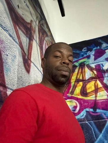 Man in red shirt standing by graffiti wall.