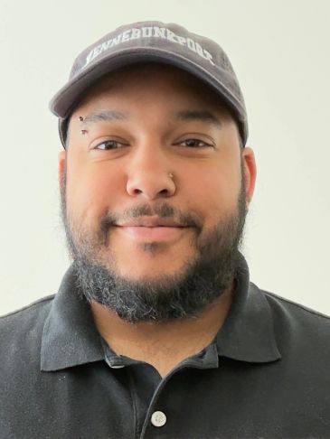 Man with a beard wearing a cap and black shirt.