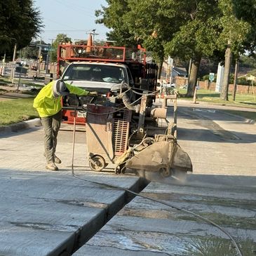 Worker cutting a concrete slab on a sunny day with heavy machinery.