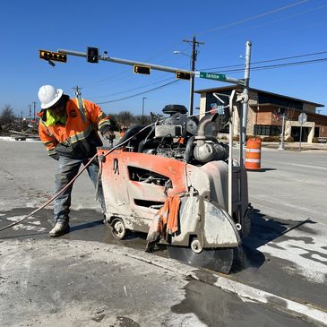 Construction worker cutting concrete with a large saw on the street.