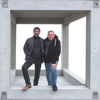 Two men posing inside a large concrete square frame.