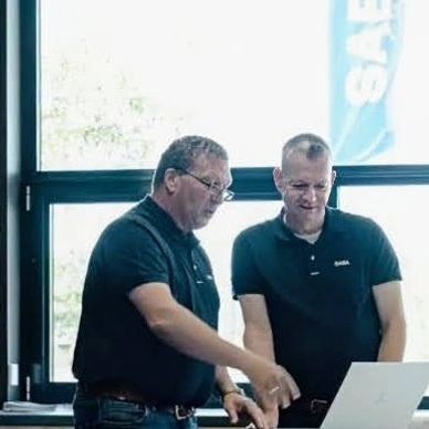 Two men in black shirts discussing something on a laptop.