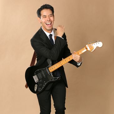 Man in suit joyfully playing electric guitar against brown background.