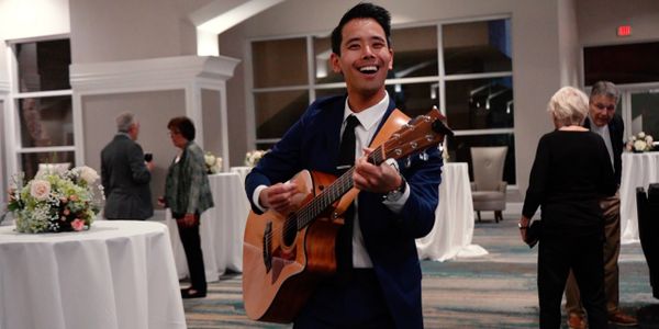 Man in suit joyfully playing acoustic guitar at a social event.