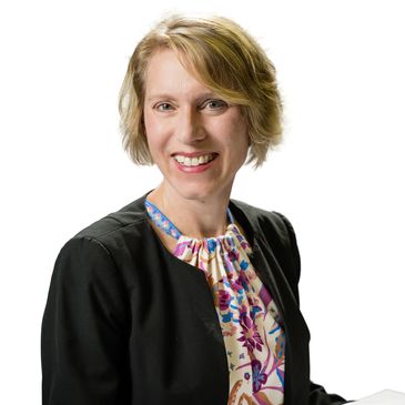 Smiling woman in a floral blouse and black jacket.