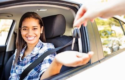 Smiling teenager holds out hand for car keys while sitting in a car