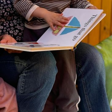 Child reading a book with an adult's help.